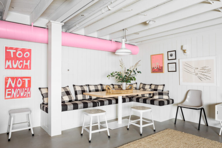 A cozy and inviting basement remodel featuring white walls with pink piping, checkered cushions on built-in seating, and a rustic wooden table.