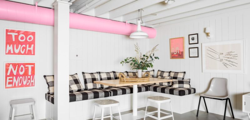A cozy and inviting basement remodel featuring white walls with pink piping, checkered cushions on built-in seating, and a rustic wooden table.